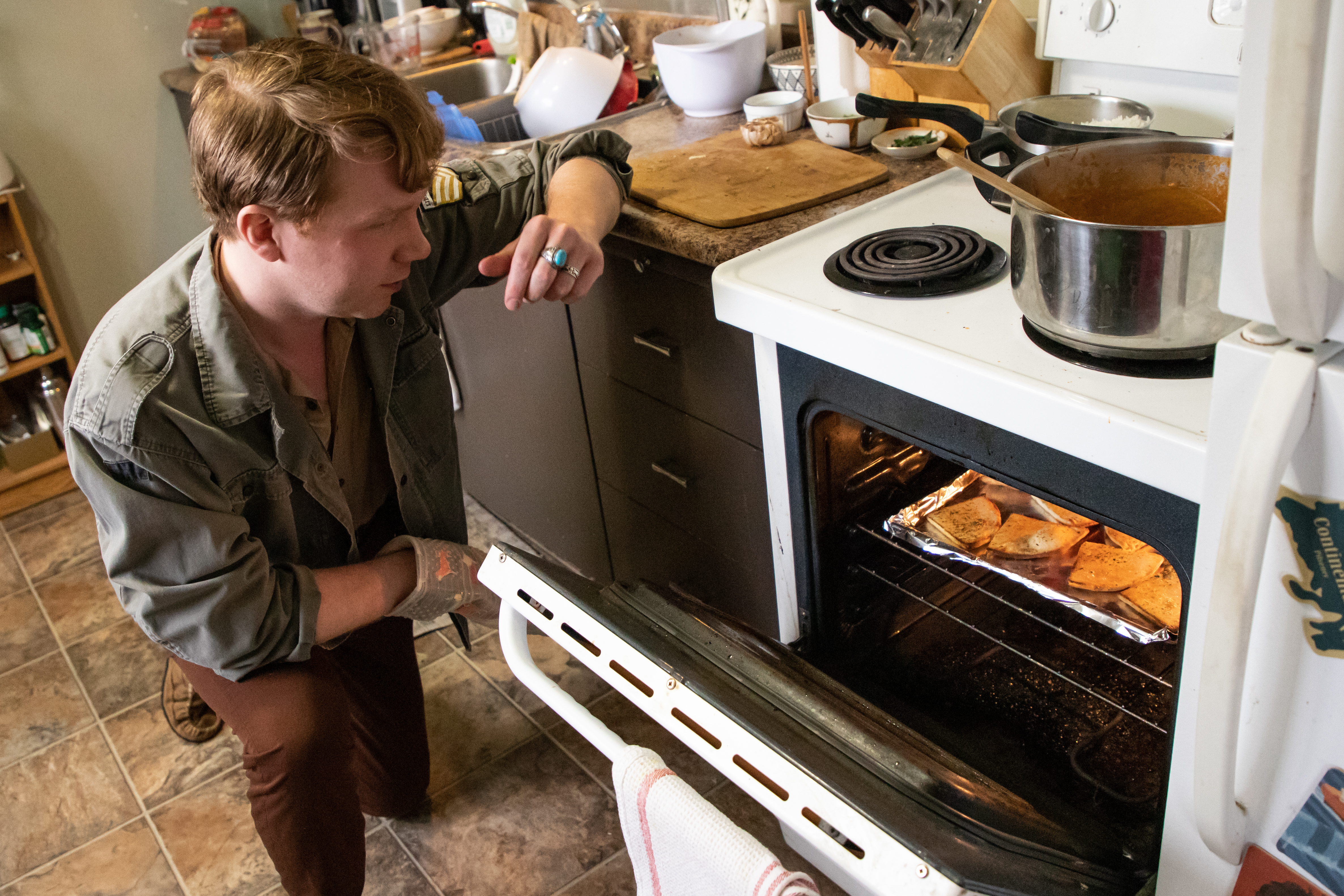 Brock kneels beside an open oven to check on his garlic naan